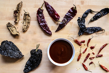 Dried ancho, guajillo, árbol and pasilla chiles beside a bowl of red chile sauce